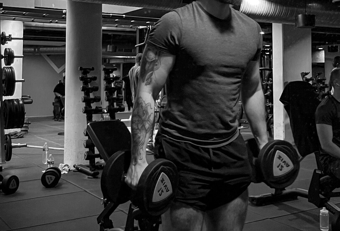 Coach sportif réalisant un exercice avec haltères dans une salle de musculation, travail spécifique pour le renforcement du dos